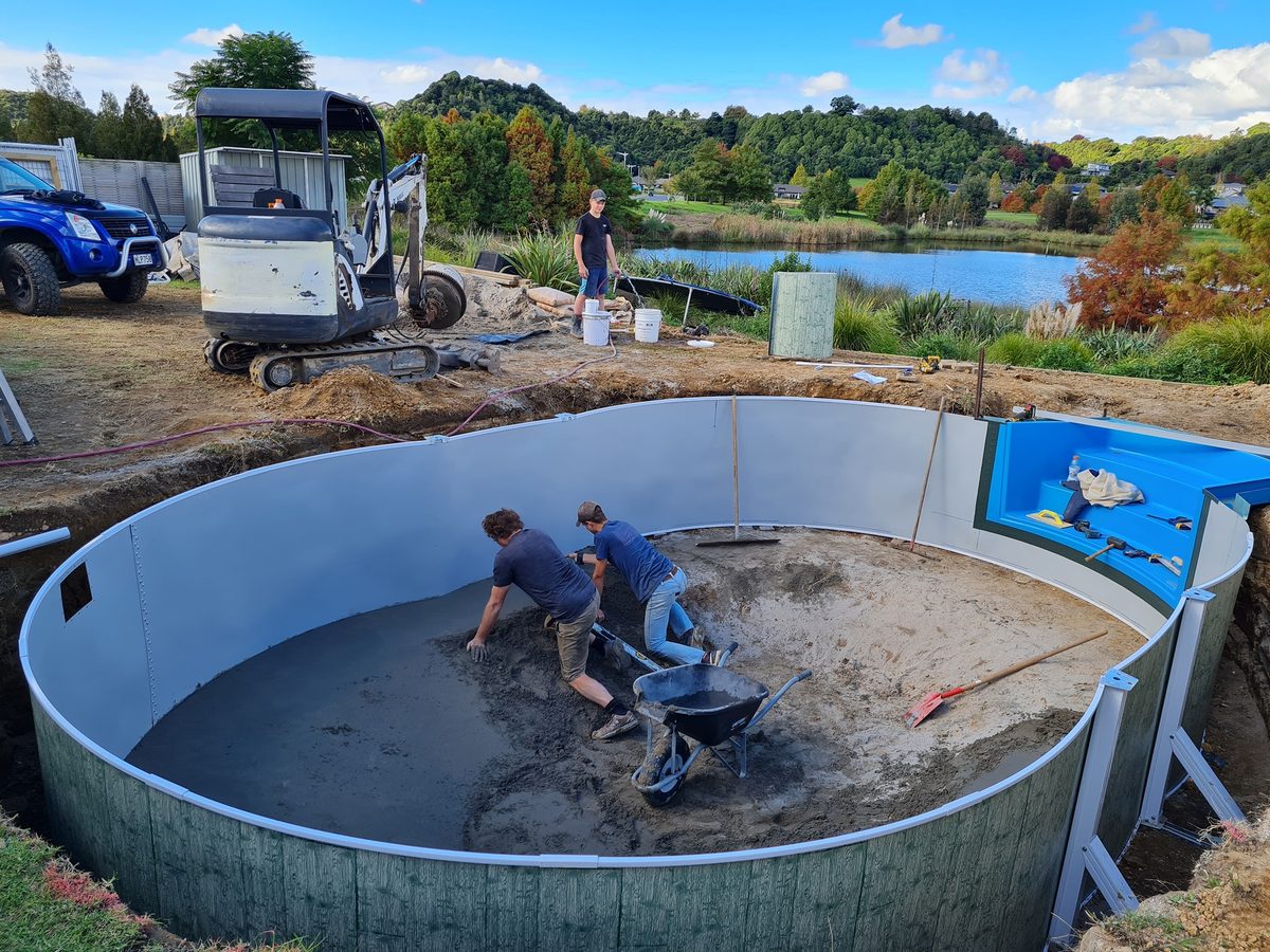 Two men levelling the floor inside a curved pool wall during a build