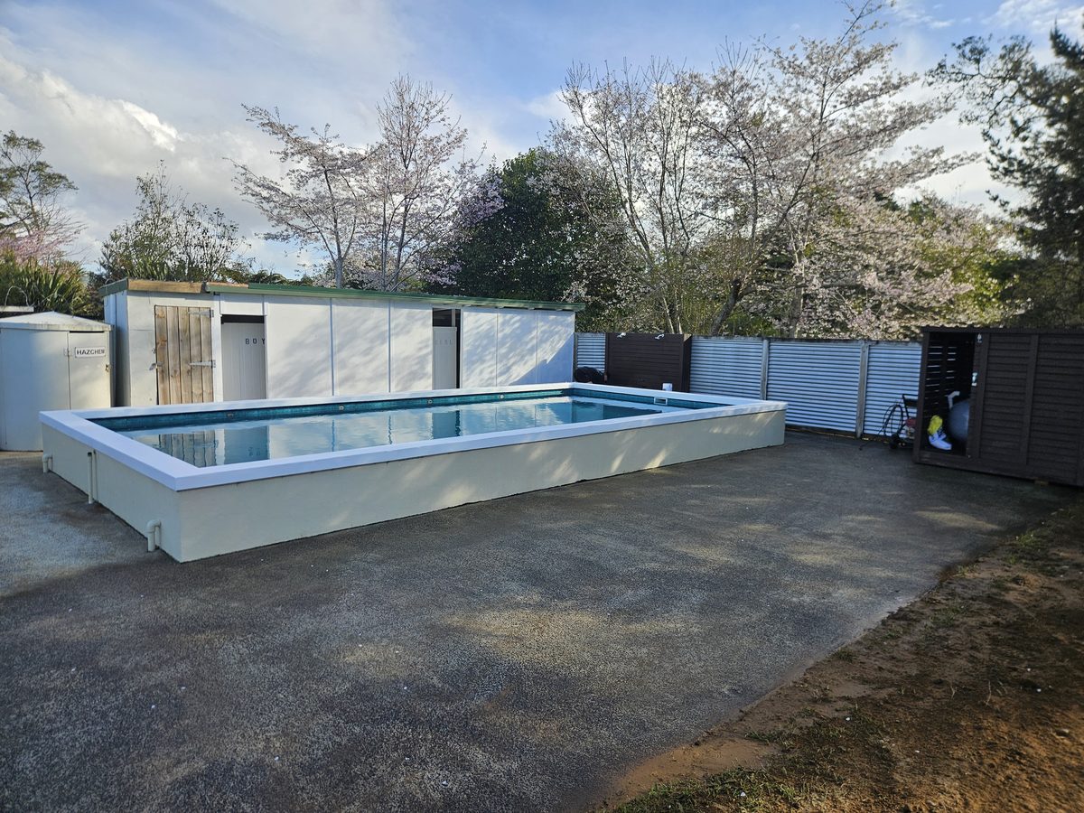 A raised rectangular pool with a white surround on a gravel yard