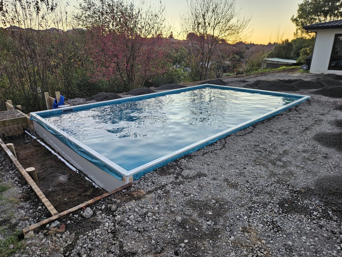 A new rectangular pool filling with water at dusk, the ground around it still bare