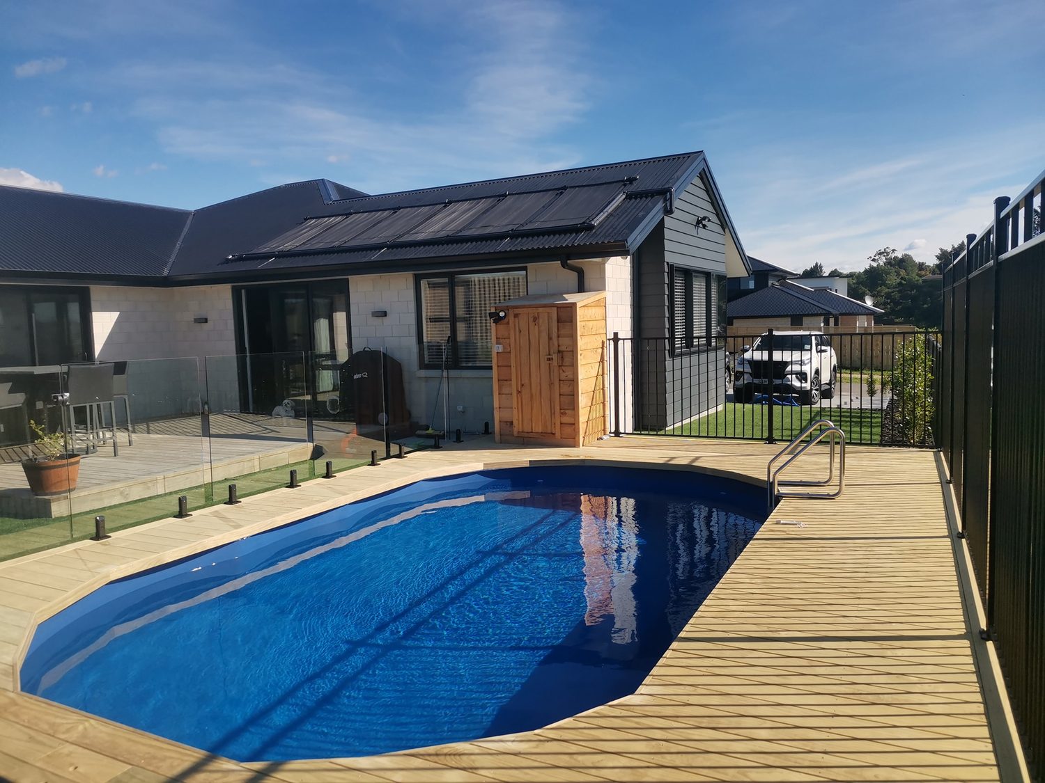 A pool set into a timber deck in front of a house with solar panels on the roof