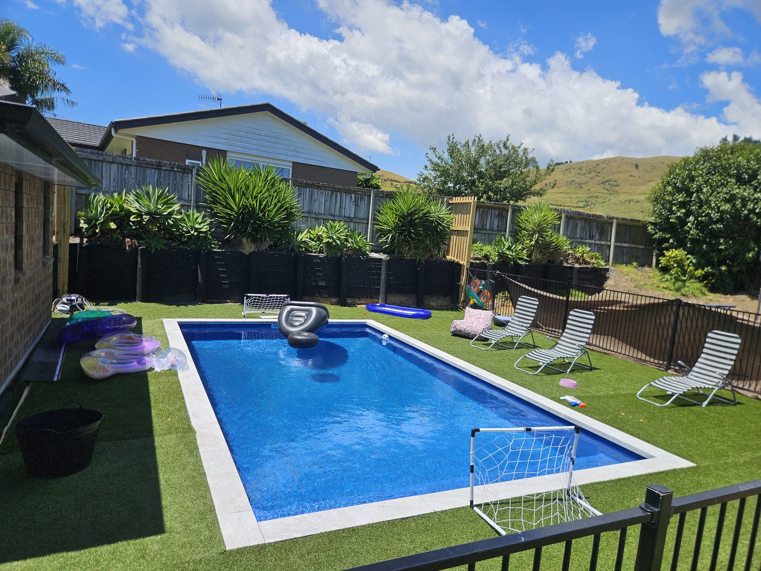 A rectangular pool surrounded by artificial grass with loungers and a black fence