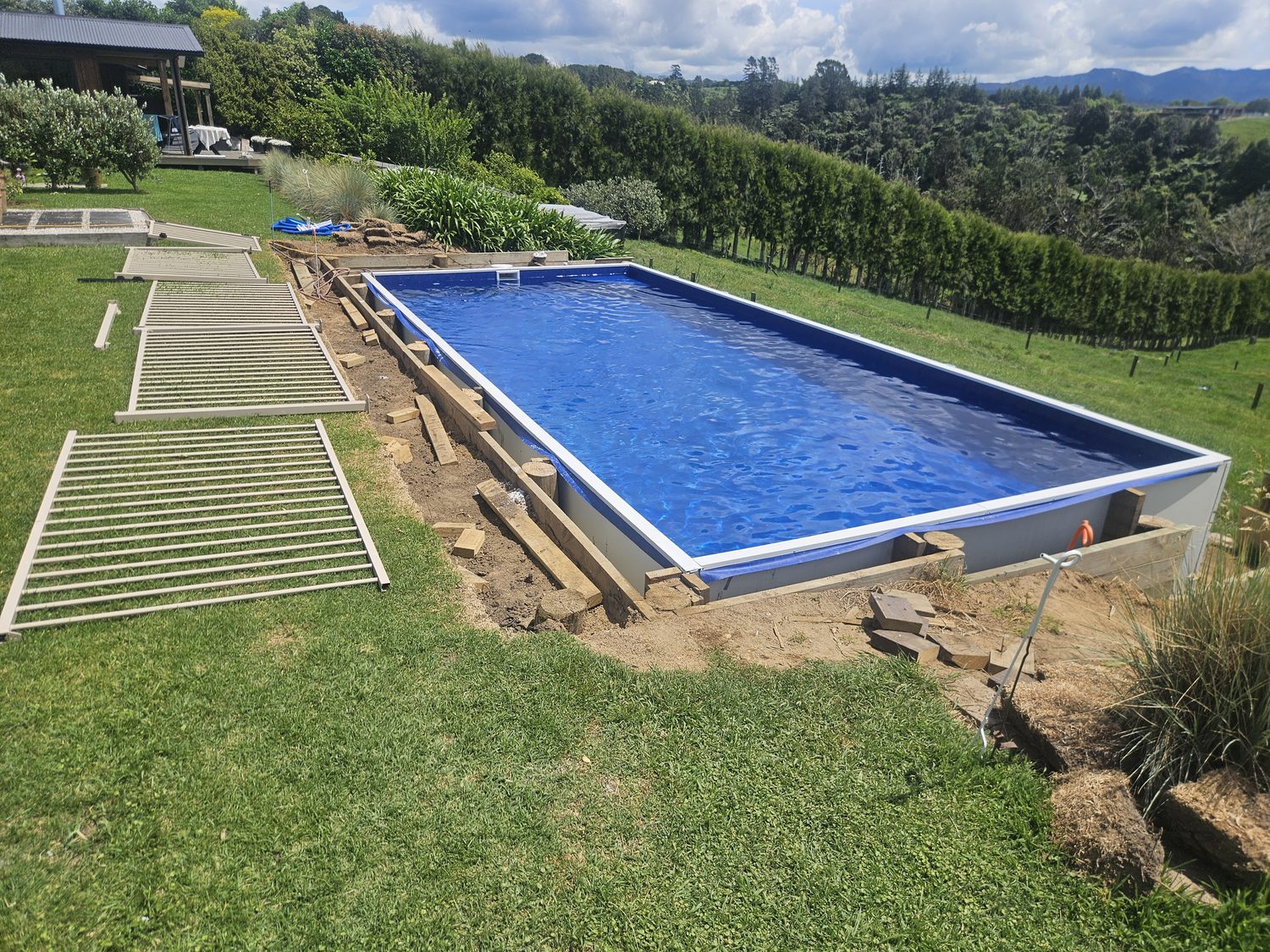 A long rectangular liner pool in a lawn with bush-covered hills behind