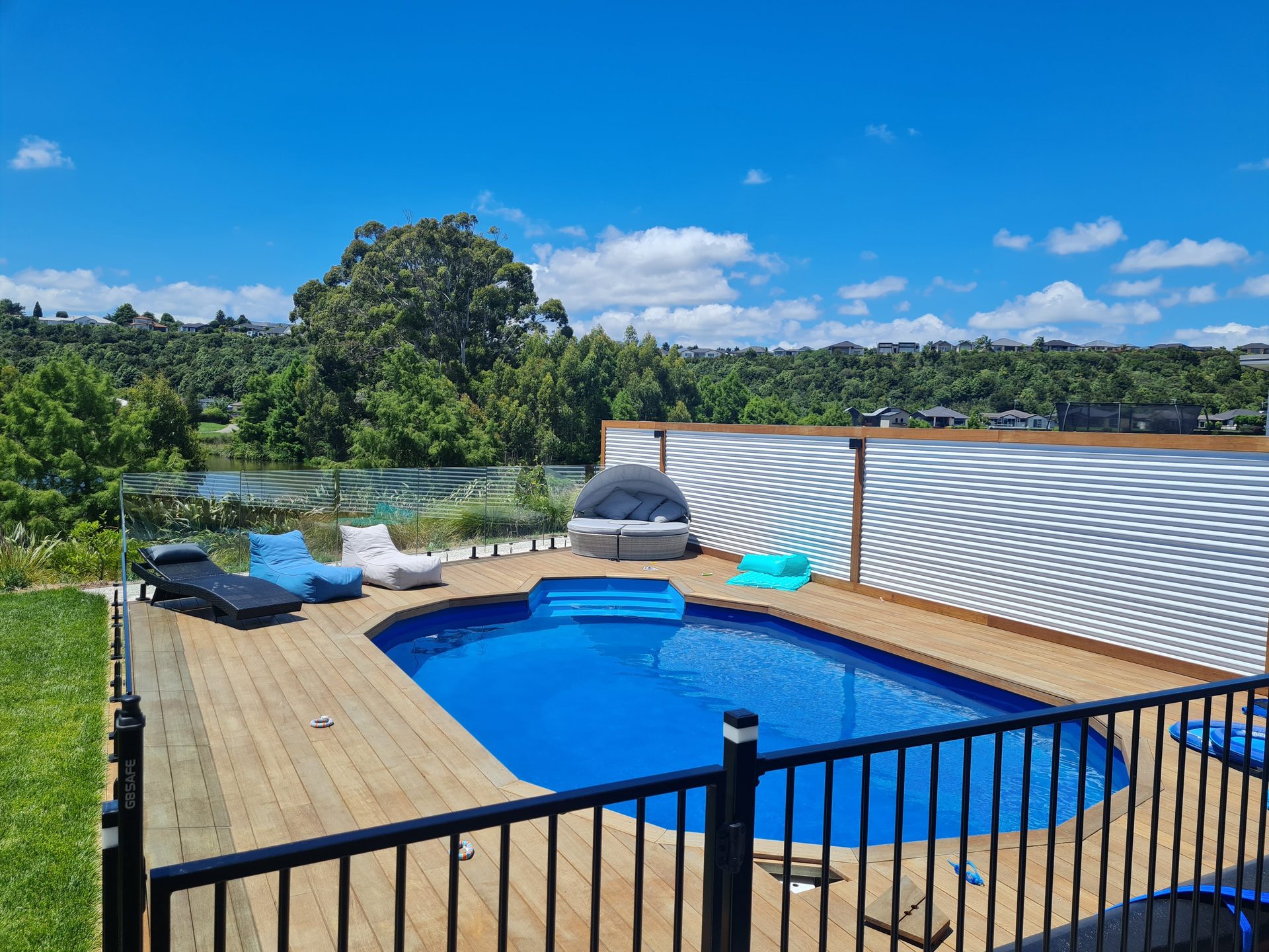 A pool in a timber deck behind a black aluminium fence, looking out to water and trees