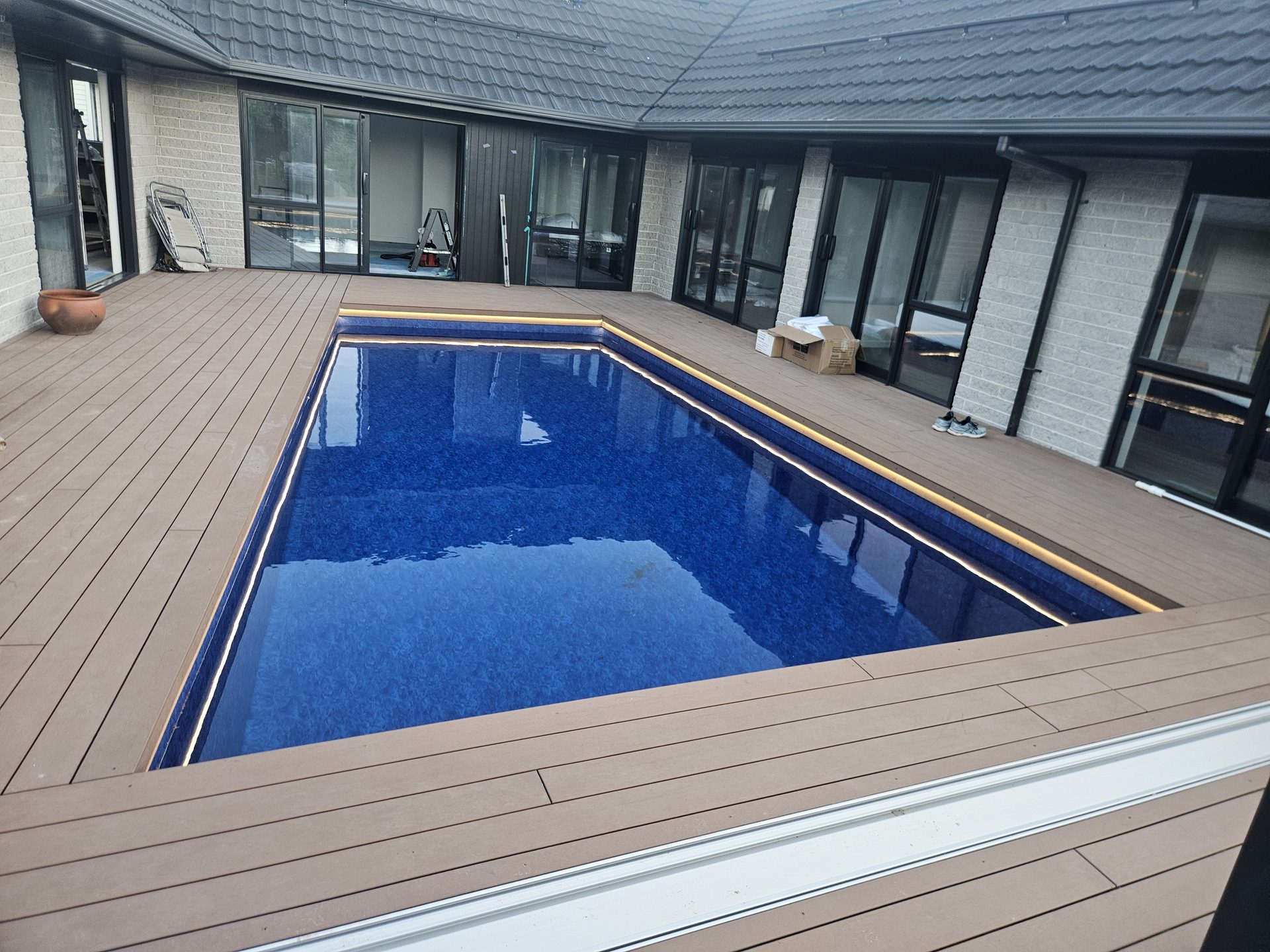 A rectangular pool with a dark blue liner set into a timber deck beside a house
