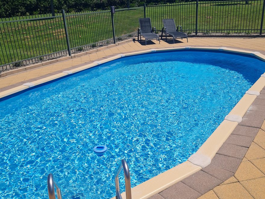 A pool with clear water, a stainless steel ladder and a paved surround